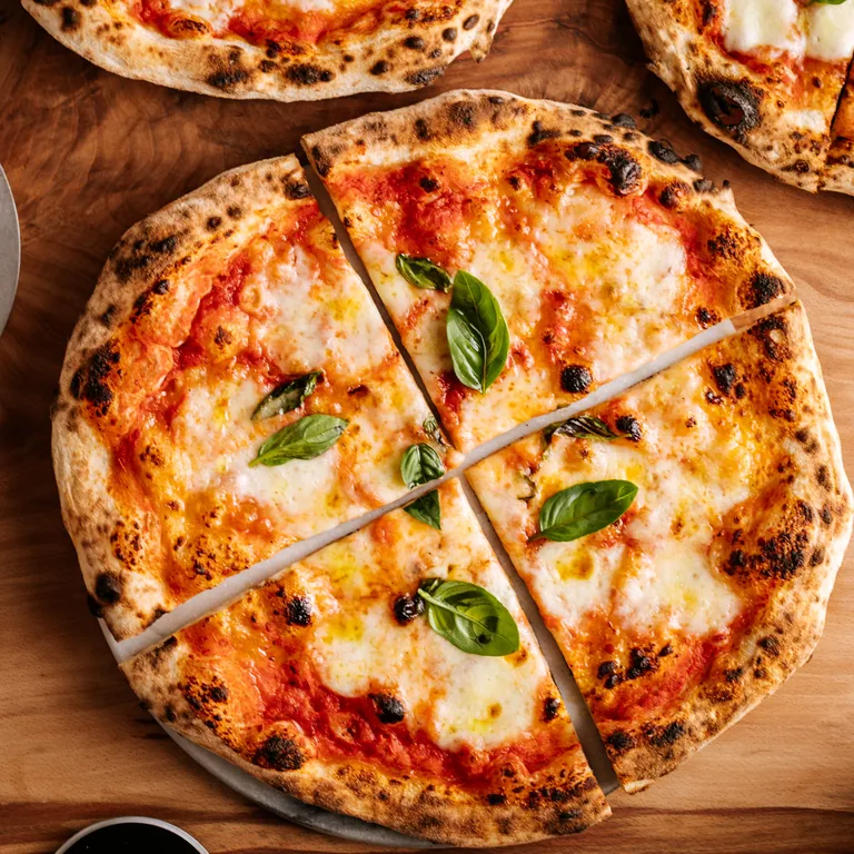 Finished Neapolitan pizza with a blistered rim, tomato, mozzarella and basil