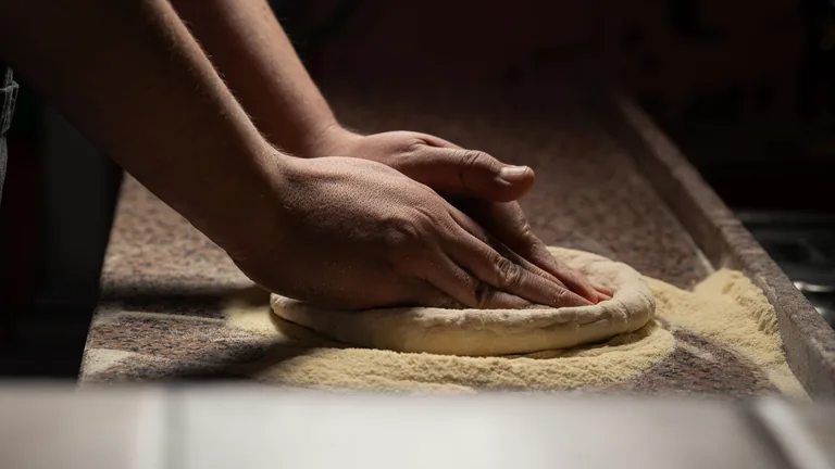 Hands pressing pizza dough from the centre while preserving the raised rim
